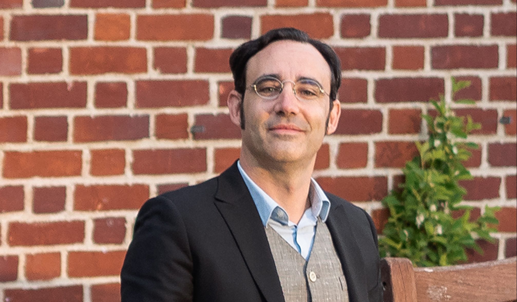 a man with glasses in a wheelchair in front of a brick wall