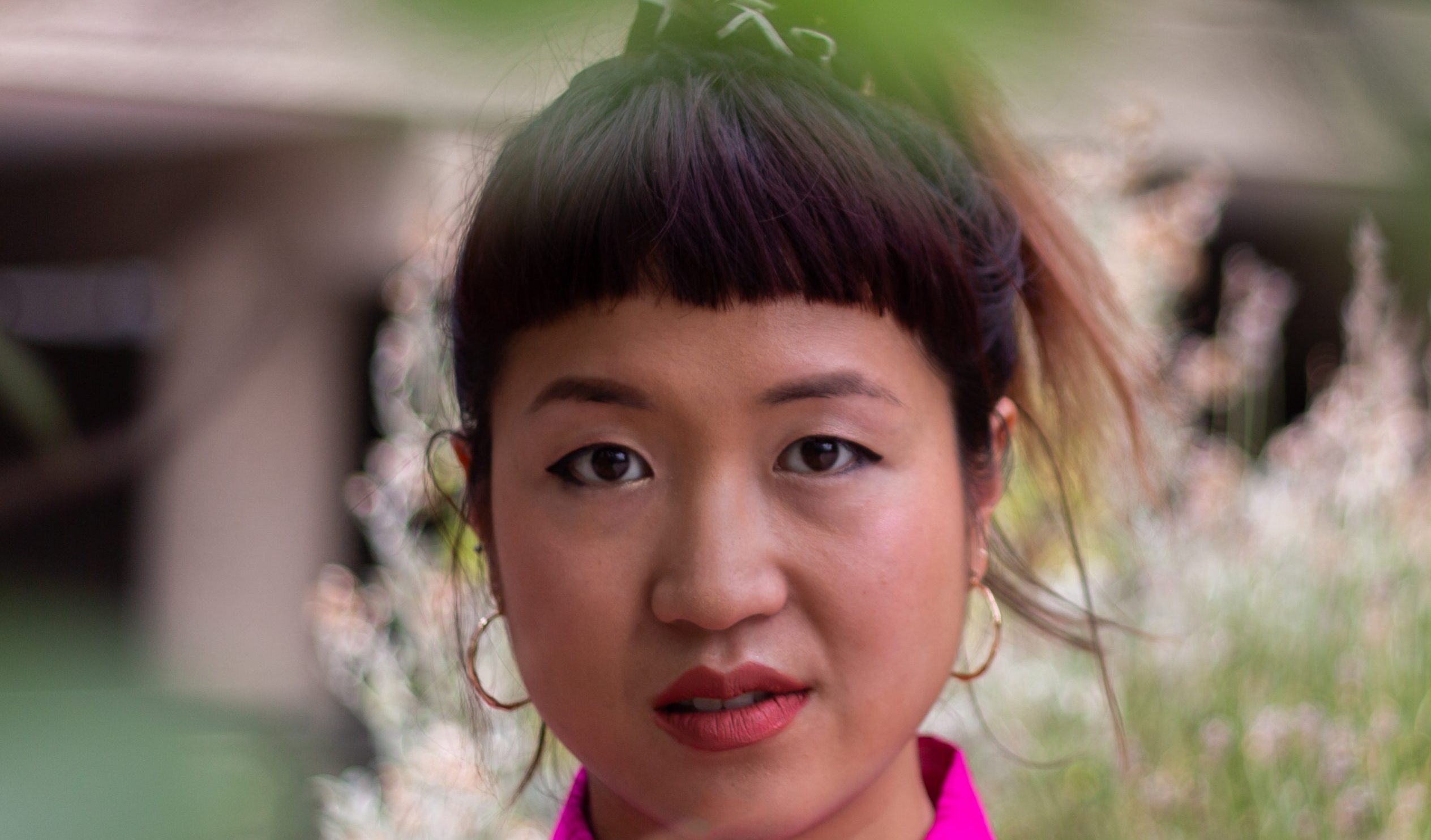 a person in a bright pink shirt looking at the camera in front of trees