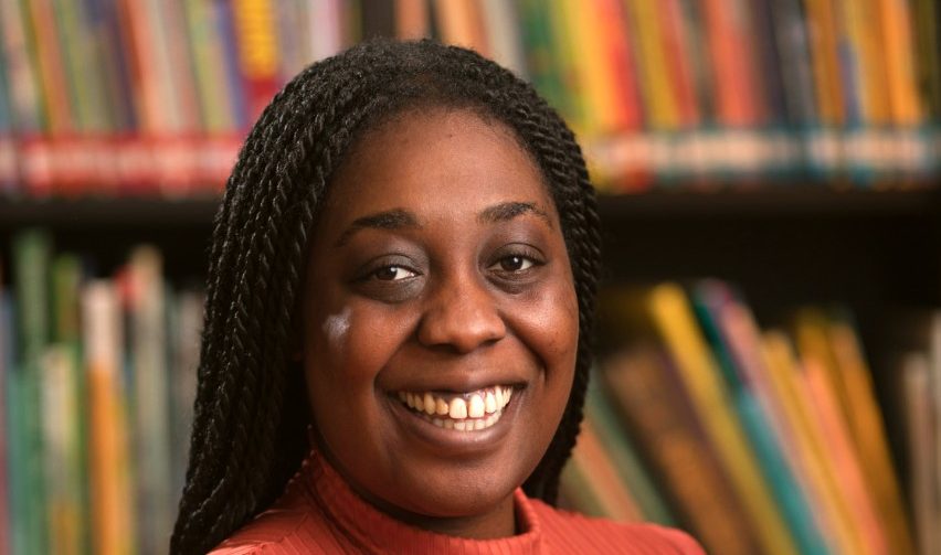 photo of a person with a big smile and read jumper in front of a bookcase