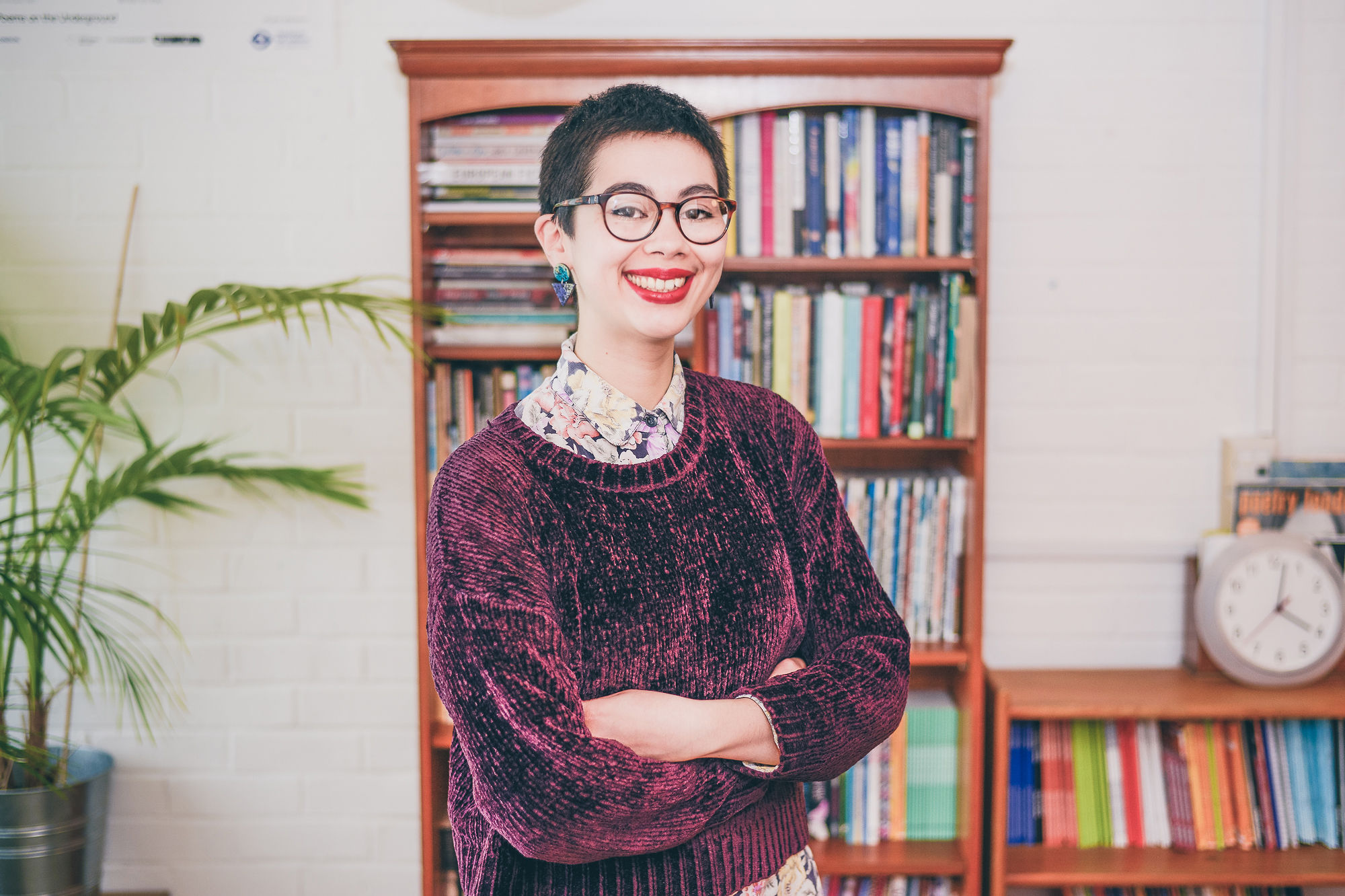 a person with short hair, glasses and red lipstick smiling in front of a bookcase