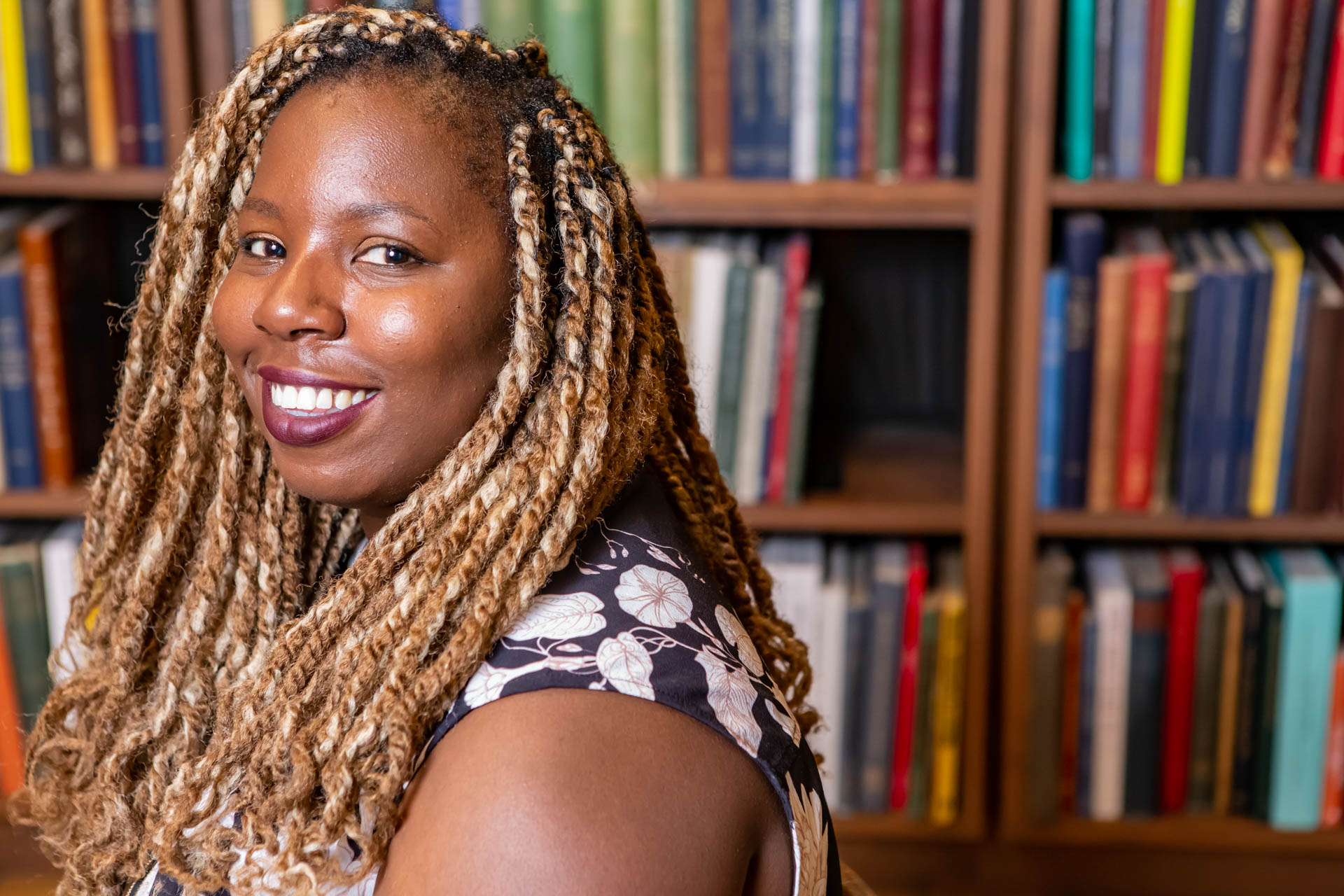 a person looking to the side and smiling in front of a bookcase