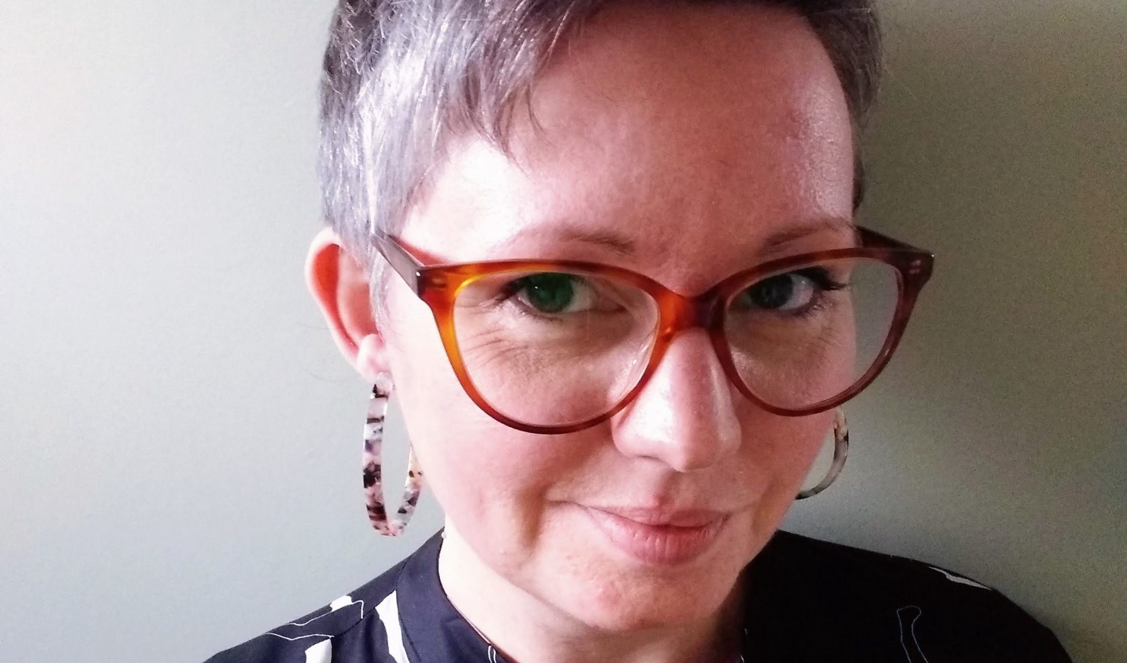 a woman with short hair, wearing big tortoiseshell glasses and earrings smiling at the camera