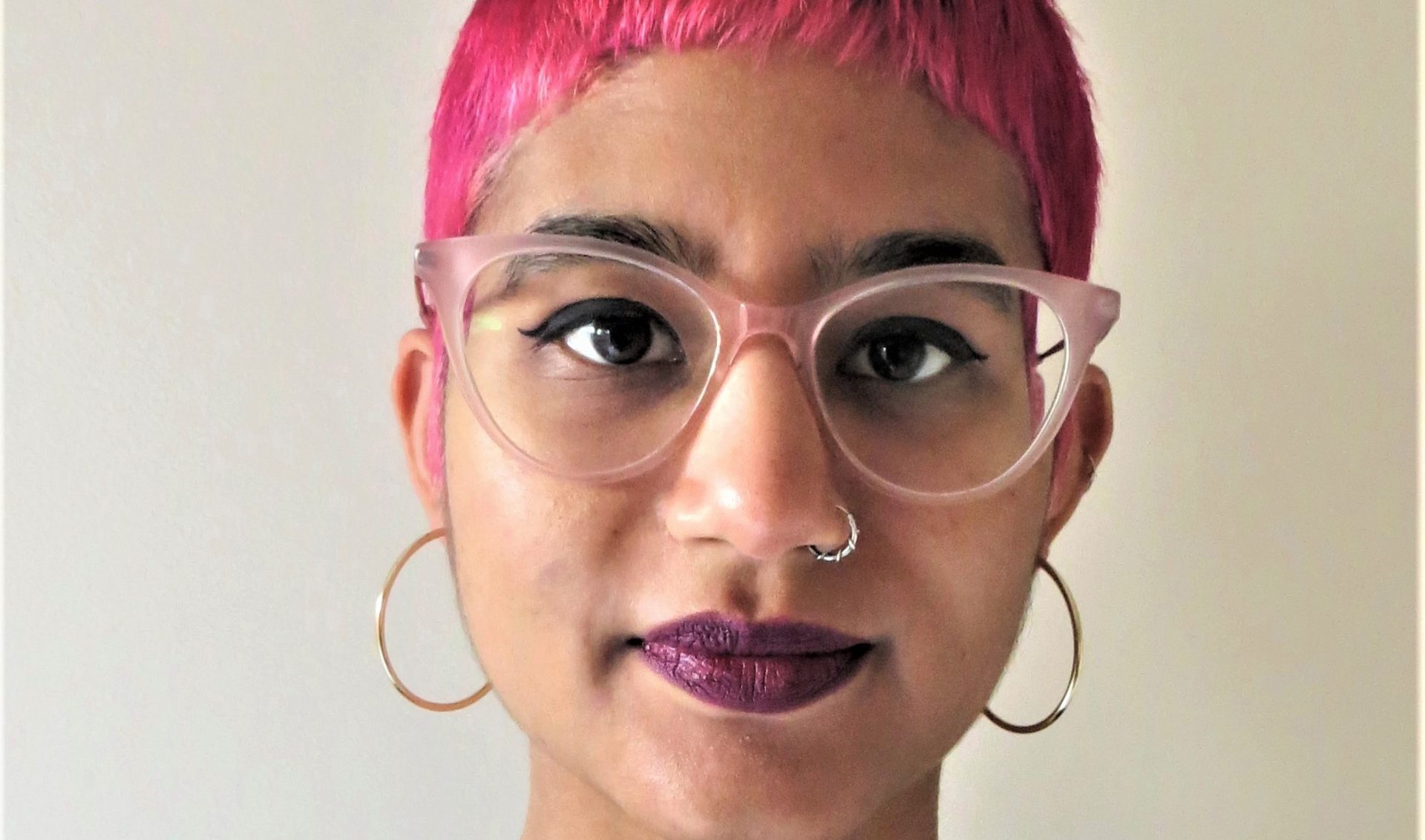 a person with pink hair and big pink glasses looking at the camera