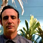 An author looking serious with tropical plants in the background.