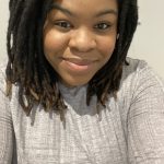 a close up photo of a woman's face, her hair is braided and she is smiling