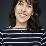 a photo of a woman wearing a black and white stripey top with shoulder length dark hair smiling widely at the camera