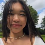 a closeup of a woman with long dark hair wearing a beaded choker and a white tshirt