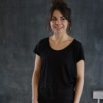 a woman with her hair in a bun wearing big hoop earrings and wearing a black tshirt and trousers