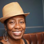 a person sitting on a sofa wearing a straw hat and smiling widely at the camera