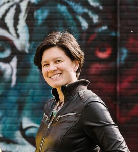 An image of a woman's head and shoulders standing sideways against a mural background