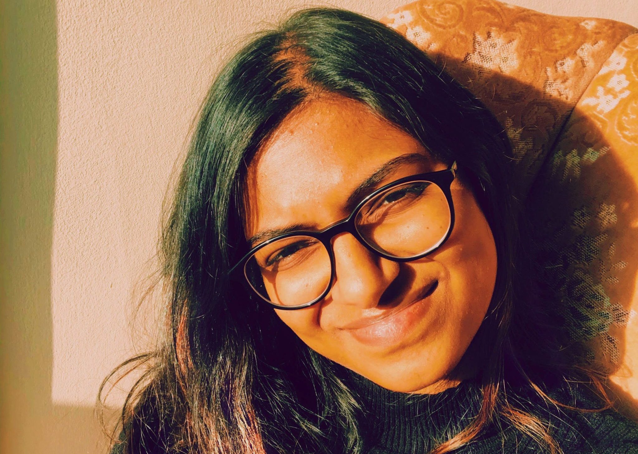 a woman with dark hair and black-framed glasses smiling
