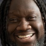 a black man with a beard smiles widely at the camera