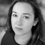 A black and white headshot of a white-passing woman with long dark hair, wearing a sleeveless dark top.