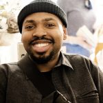 A picture of a black man with a wide smile wearing a black beanie hat 